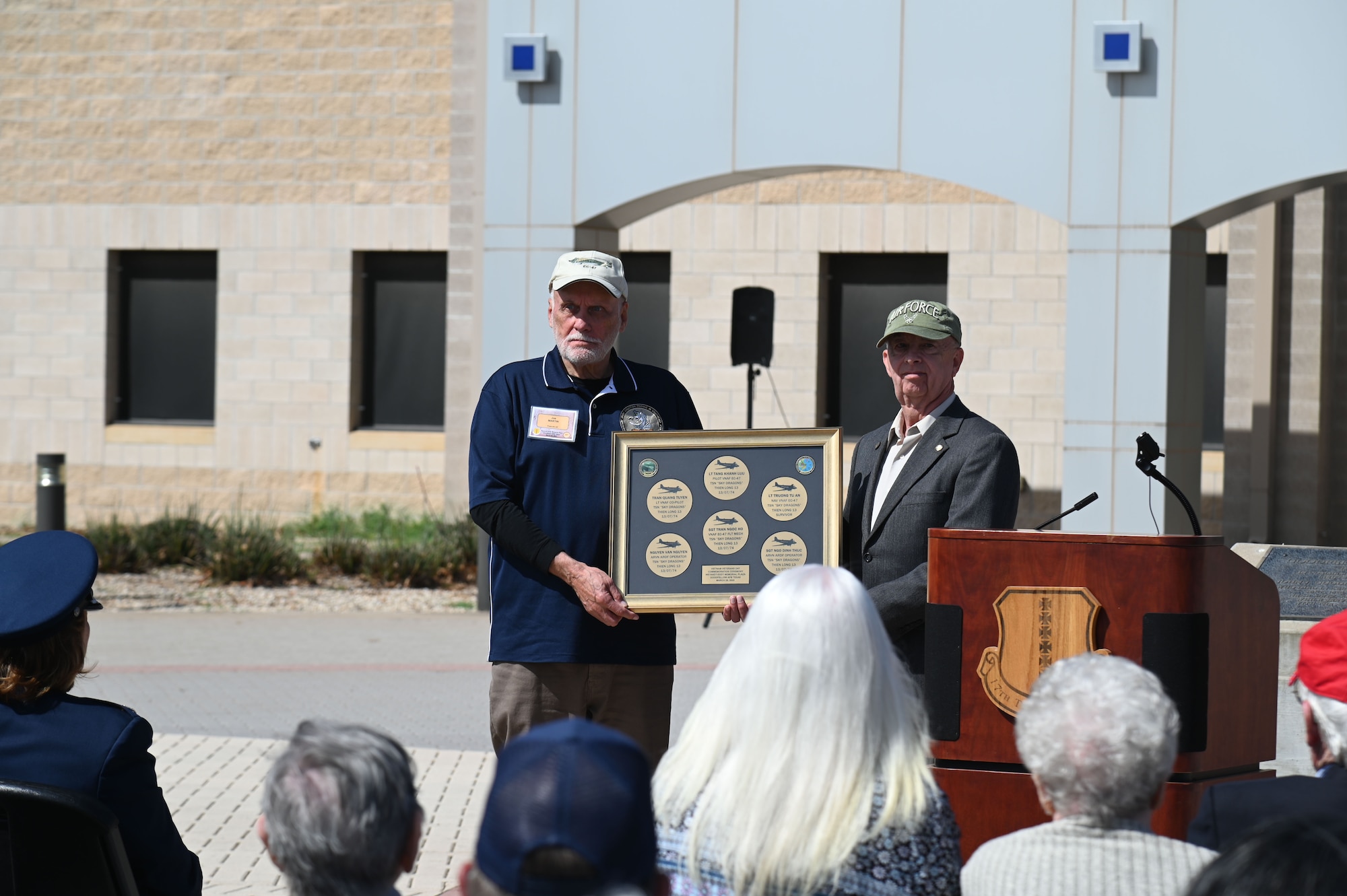 U.S. Air Force retired Chief Master Sgt. Ronald “JJ” Graham presents Joe Martin with commemorative pavers at the National Vietnam War Veterans Day Commemoration Ceremony at the Weyandt-Eddy Memorial Plaza, outside the Norma Brown Headquarters building, Goodfellow Air Force Base, Texas, March 28, 2025. The five bronze pavers shown are in honor of the five members of the Vietnamese EC-47 crew that was shot down by North Vietnamese troops shortly after the Americans turned over the program to the South Vietnamese. (U.S. Air Force photo by Airman 1st Class James Salellas)