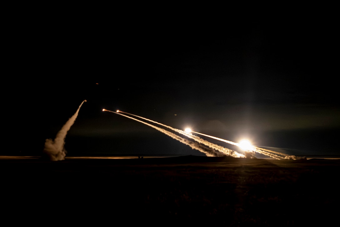 Five rockets launch into a night sky leaving behind streaks of smoke.