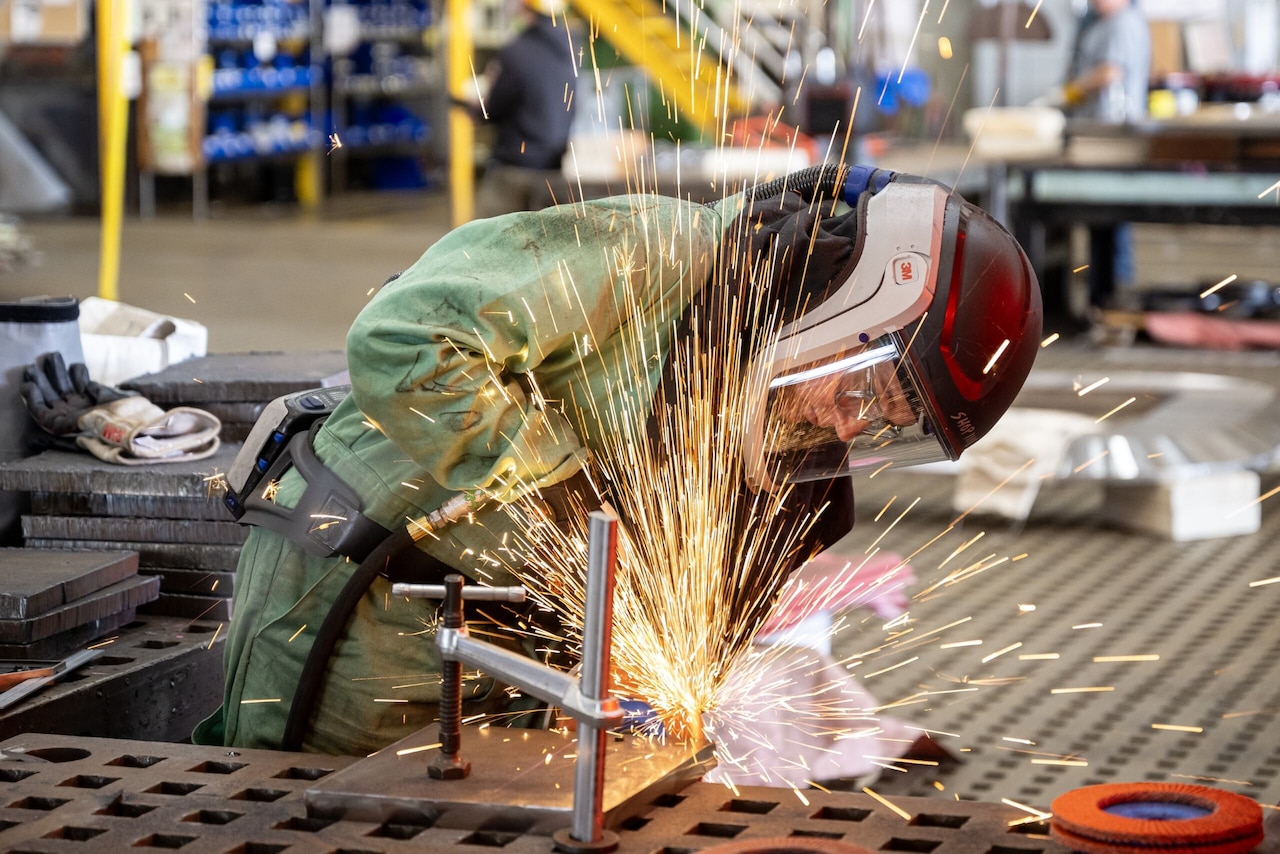 Sparks fly as a person in protective gear welds a piece of steel.
