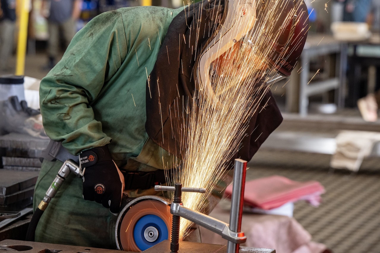 Sparks fly as a person in protective gear welds a piece of steel.