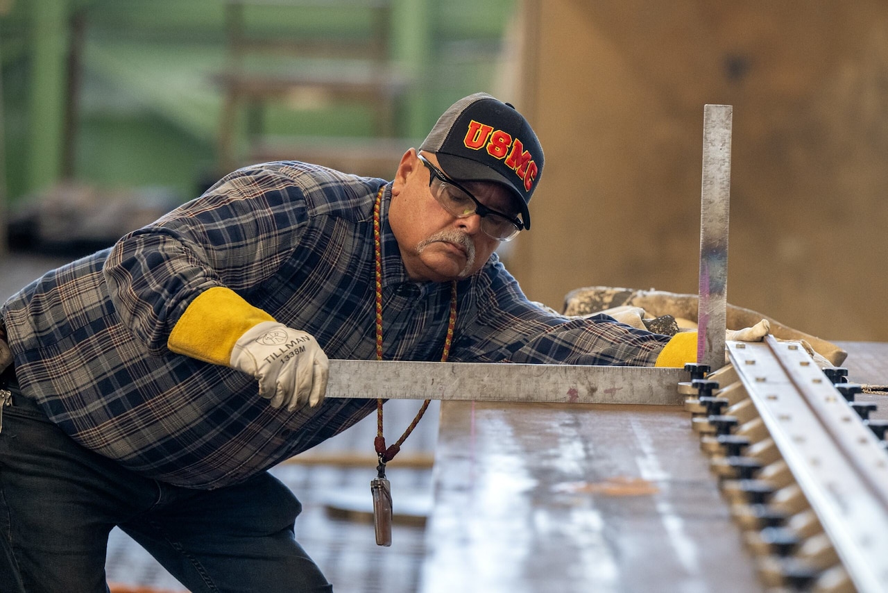 A man looks at a metal ruler placed on a piece of steel.