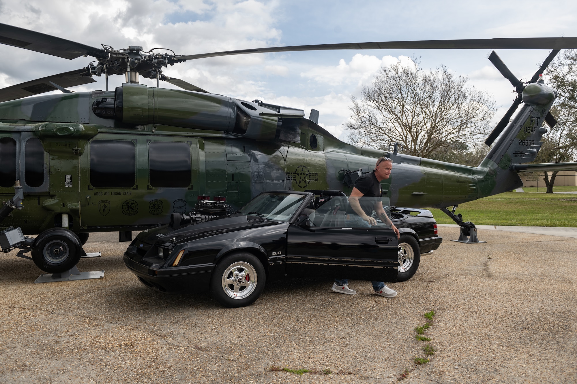 A man parks a Mustang in front of the HH-60.