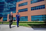 An Air Force officer in dress uniform walks next to a man in a suit.