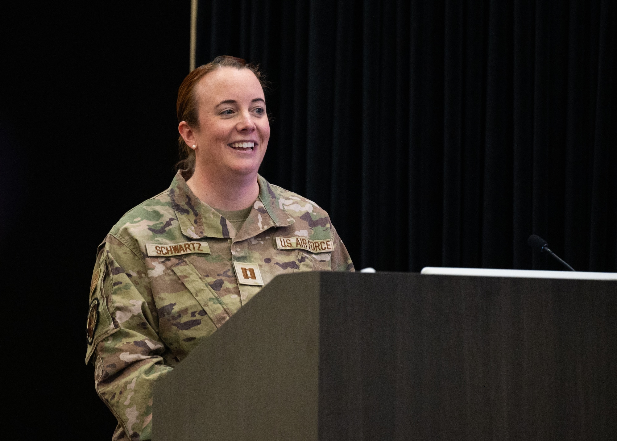 A female service member smiles while standing behind a podium
