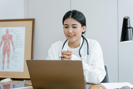 Woman in white lab coat speaks on a laptop.