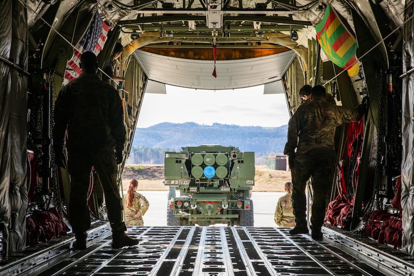 U.S. Airmen assigned to 86th Airlift Wing stand watch over key checkpoints as a U.S. Army M142 High Mobility Artillery Rocket System assigned to 3rd Battalion, 321st Field Artillery Regiment backs onto a U.S. Air Force C-130 Hercules aircraft during cold load training on Ramstein Air Base, Germany, March 24, 2025. The training supported Operation Thunderbolt Convergence, a multinational HIMARS Rapid Infiltration  exercise designed to enhance precision fires and interoperability across NATO forces. (U.S. Army photo by Spc. Hunter Carpenter)
