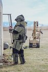 Man in EOD Bomb Suit scans building with phone with robot in the background