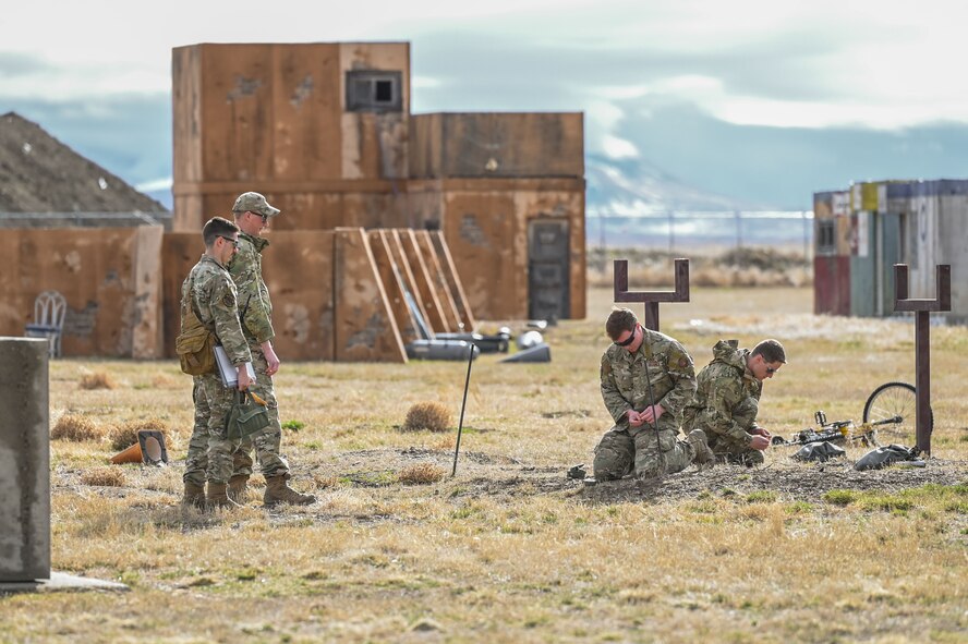 Two Airmen watching another two Airmen on their knees as they put together a device.