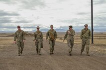 Five Airmen walk alongside each other outside with mountains in the background.
