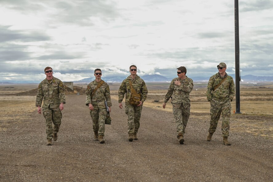 Five Airmen walk alongside each other outside with mountains in the background.