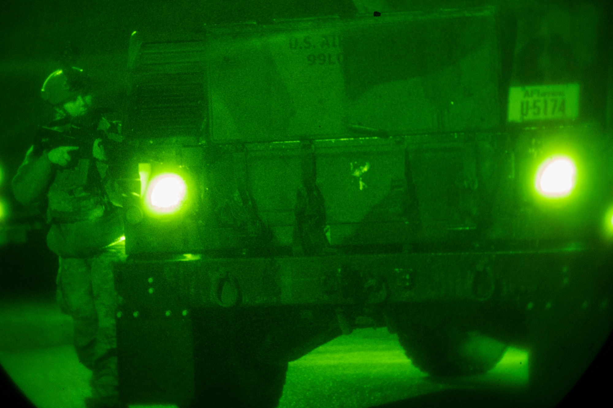 An armed Airman leans out from behind an armored vehicle
