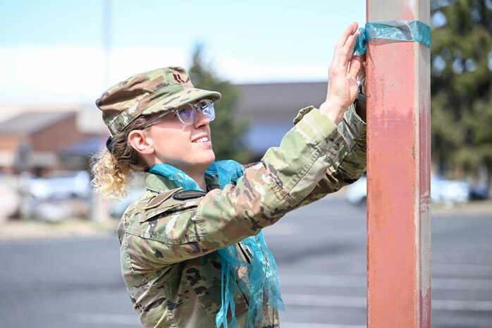 An airman ties a teal ribbon on a pole