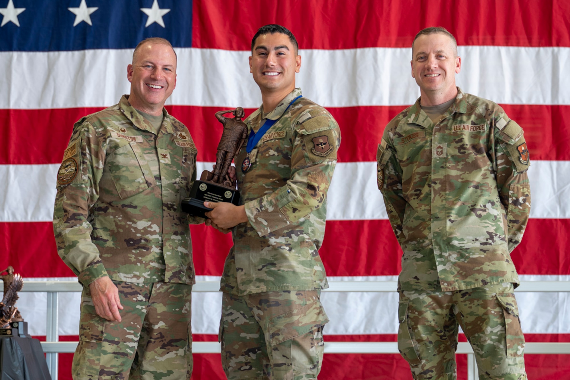 U.S. Air Force Staff Sgt. Francisco Rosales, center, accepts the Thomas N. Barnes Crew Chief of the Year Award from U.S. Air Force Col. Chris Dunston, 49th Maintenance Group commander and U.S. Air Force Chief Master Sgt. Andrew Stokes, 49th MXG superintendent, at Holloman Air Force Base, New Mexico, March 28, 2025. The Thomas N. Barnes Crew Chief of the Year Award recognizes those appointed to the position of aircraft dedicated crew chiefs who have made a significant contribution to the Air Force operational mission. (U.S. Air Force photo by Senior Airman Michelle Ferrari)