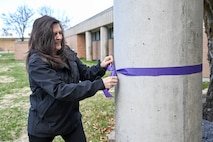 A woman ties a purple ribbon around a pole
