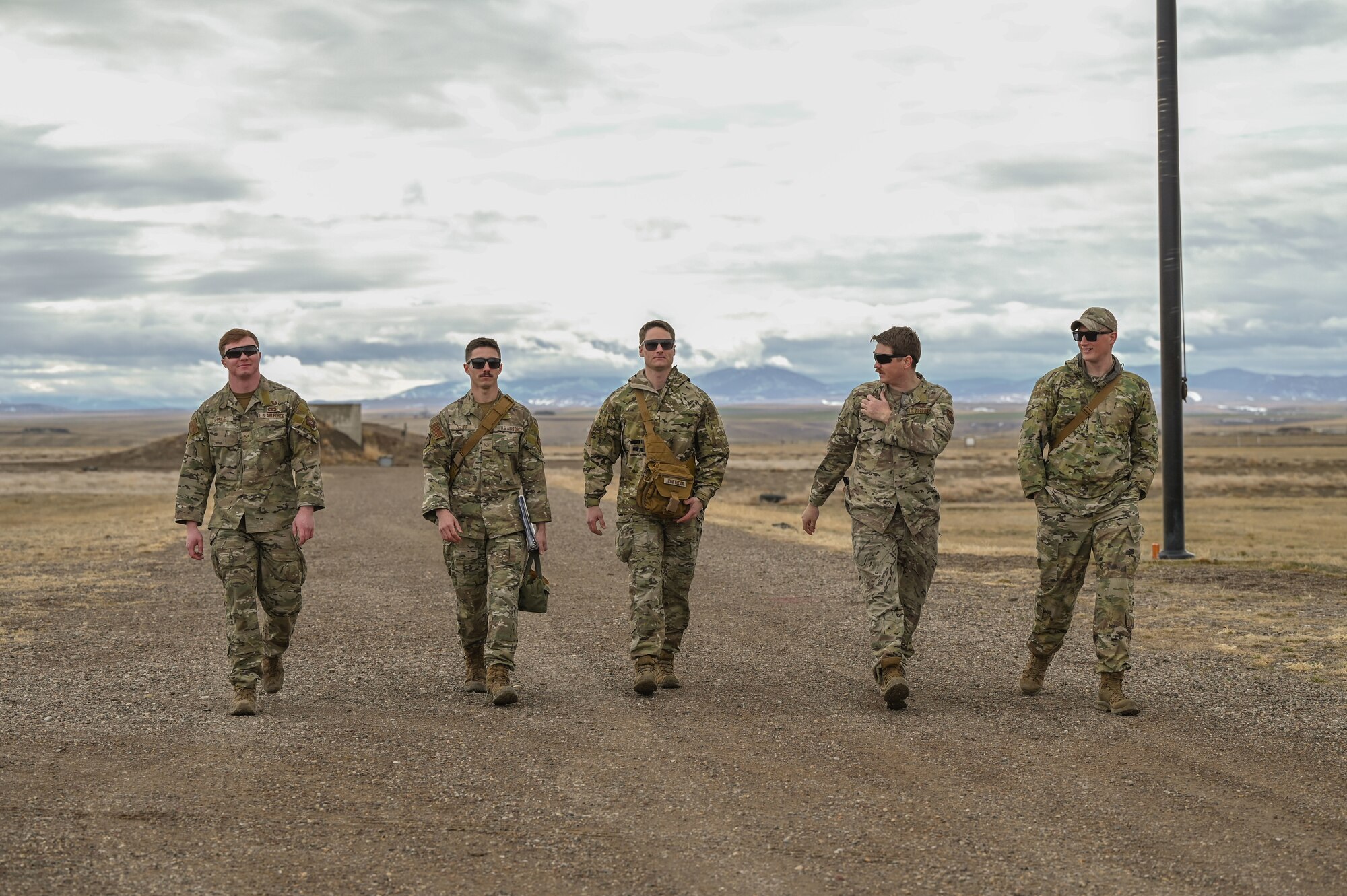 Five Airmen walk alongside each other outside with mountains in the background.