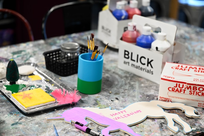 Arts and craft supplies are laid out upon a table including paint, paint brushes, and a unicorn cut out.