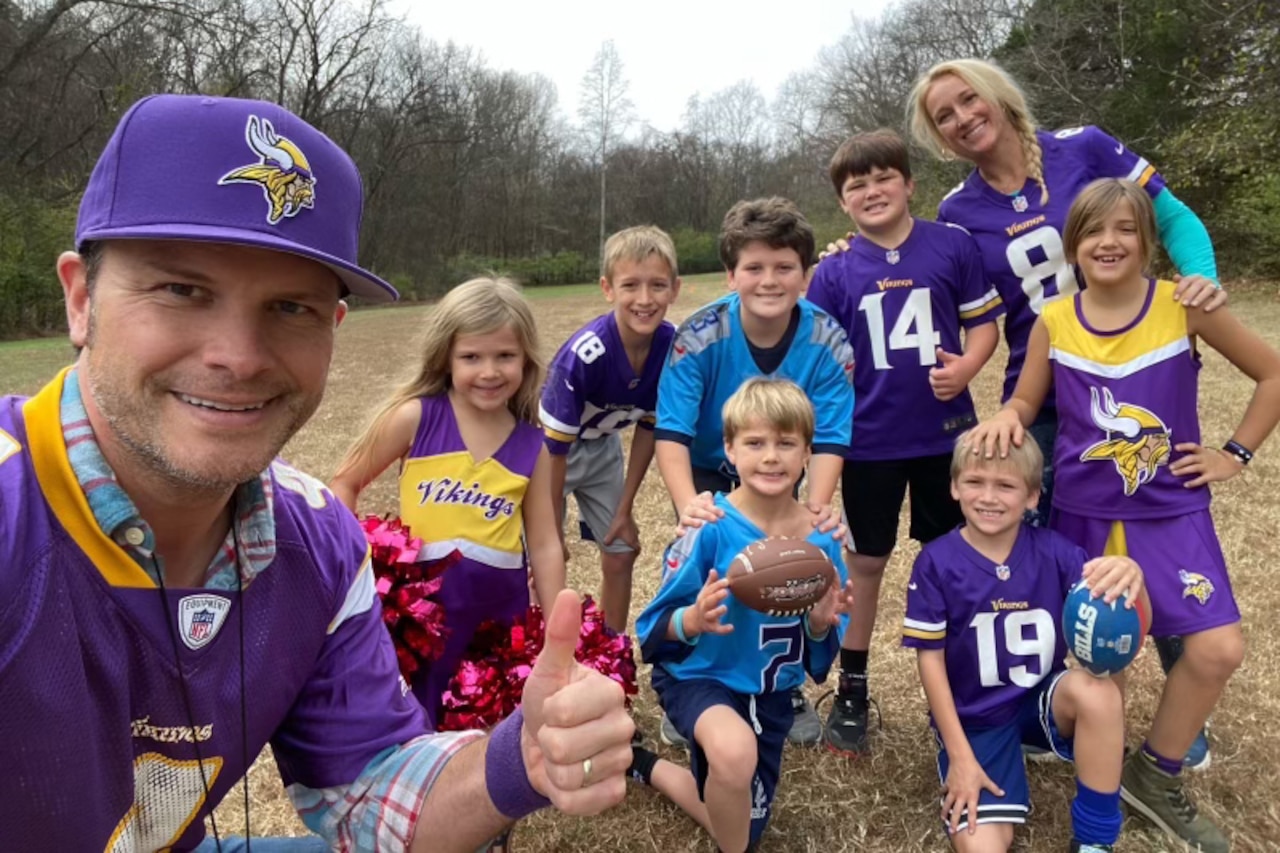 A man poses with a woman and seven children. All are wearing football jerseys.