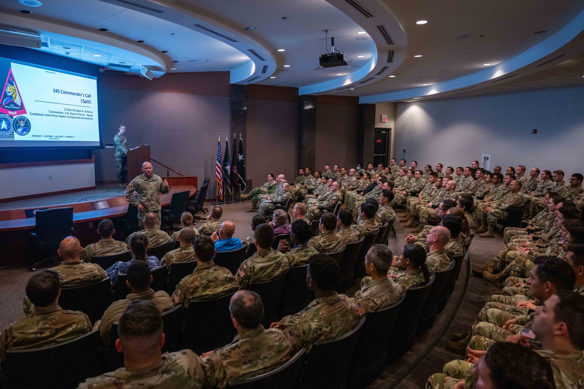 A military member speaks to a large crowd of other military members.