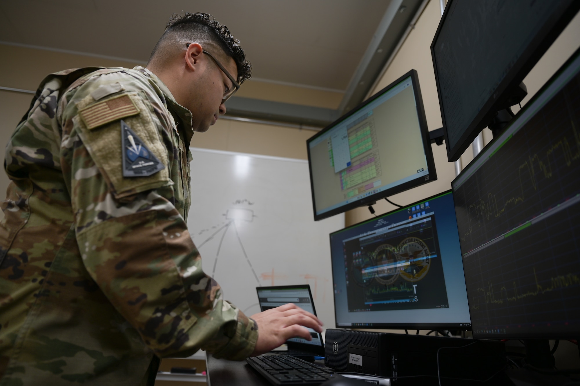 An Airman utilizing four computer screens while typing on a keyboard.