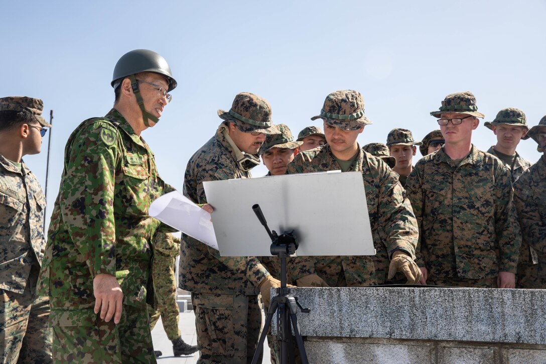 Japan Ground Self-Defense Force Maj. Mitsuo Terami, chief of the Maneuver Affairs Office, General Service Unit, JGSDF Camp Nihonbara, teaches about maintaining security at specific entry control points to U.S. Marines with Combat Logistics Squadron 36, 3rd Sustainment Group Experimental, 3rd Marine Logistics Group, during Exercise Northern Dragon at JGSDF Camp Nihonbara, Japan, March 14, 2025. Exercise Northern Dragon allowed Marines from Marine Corps Air Station Iwakuni to conduct live-fire ranges and train to maintain security in an austere environment. (U.S. Marine Corps photo by Cpl. Colin Thibault)