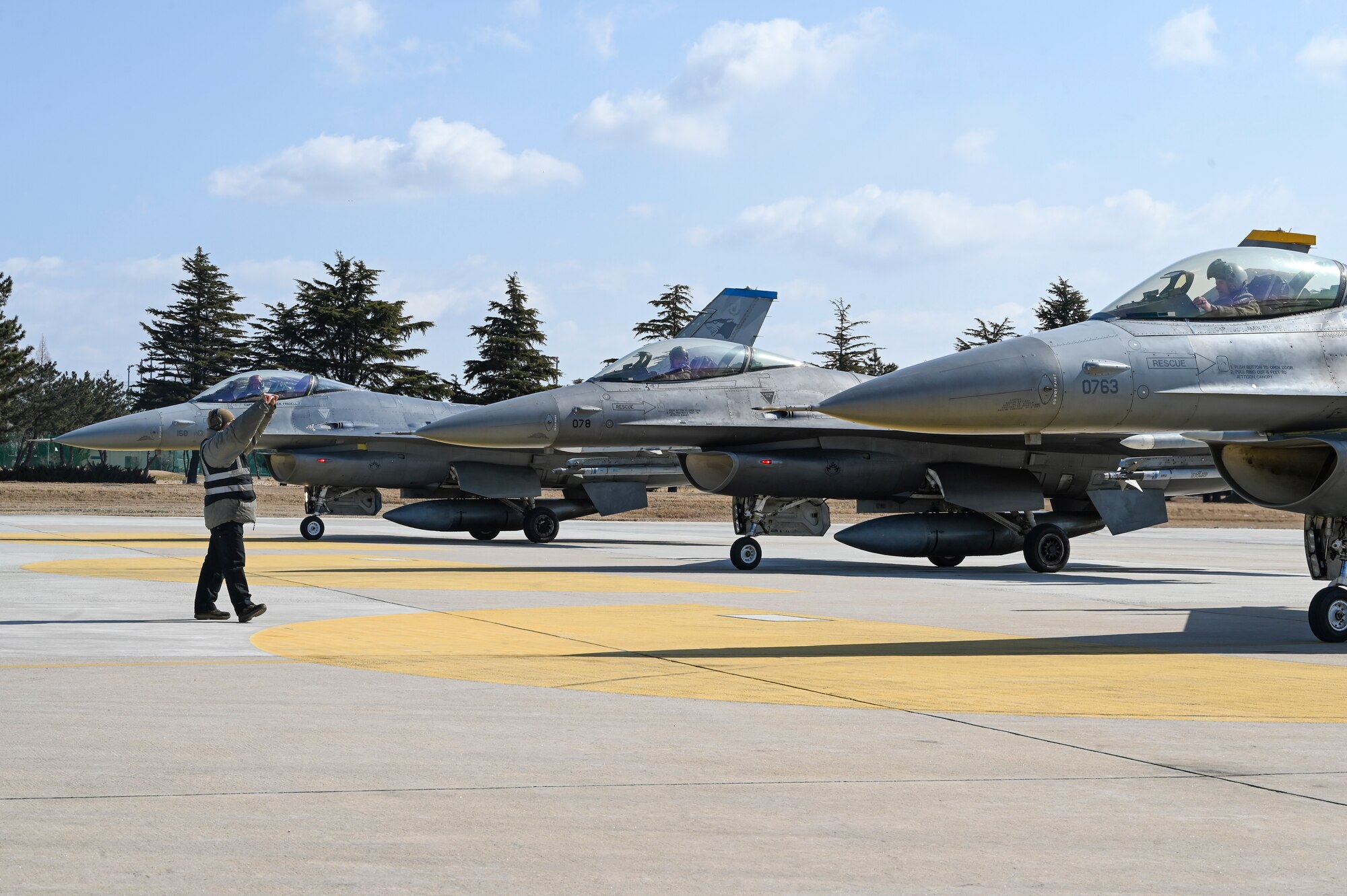 Senior Airman Jayven Nachampassek, 35th Fighter Generation Squadron dedicated crew chief, marshals three F-16 Fighting Falcon aircraft during an operational surge.