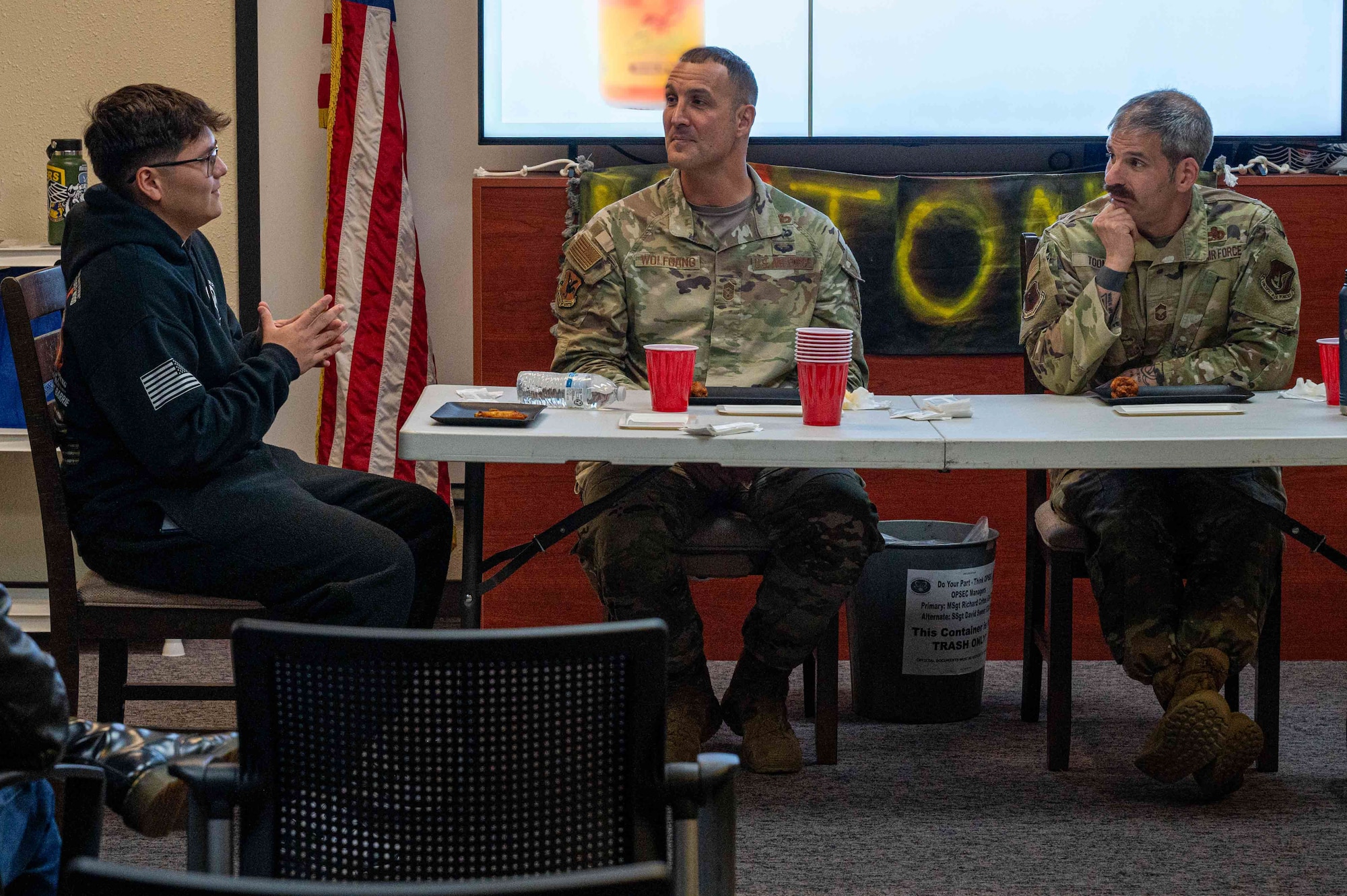 Military members sit at a table eating chicken wings