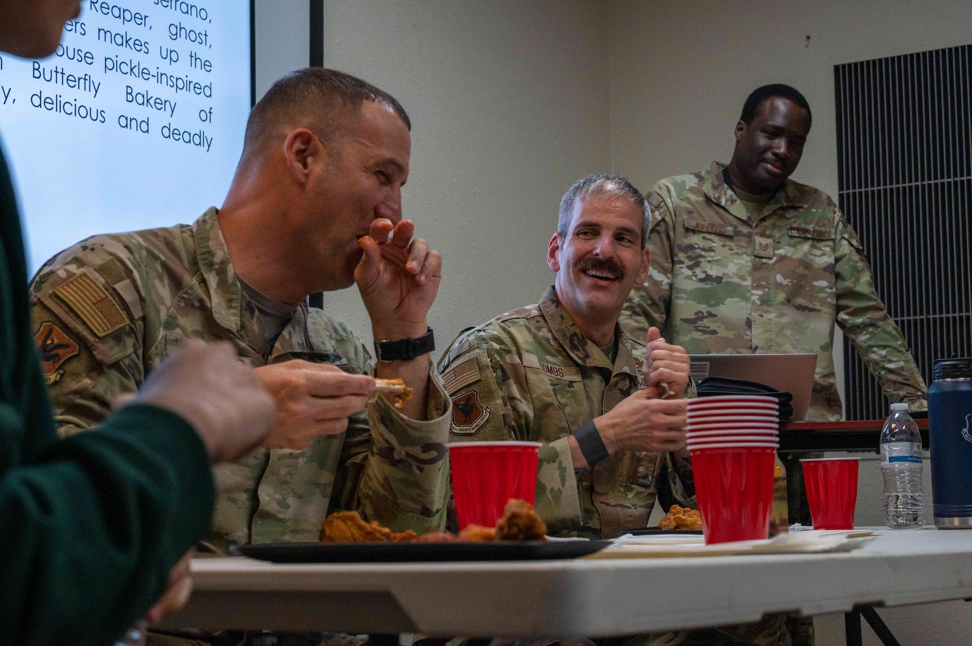 Military members sit at a table eating chicken wings