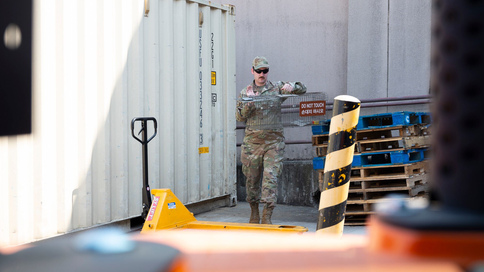 U.S. Air Force Senior Airman Aaron Burdette, 51st Civil Engineer Squadron pest manager, picks up a live-catch trap at Osan Air Base, Republic of Korea, April 1, 2025. These traps are used as a precaution to capture unwanted animals, effectively preventing possible damage to equipment and structures. (U.S. Air Force photo by Senior Airman Rome Bowermaster