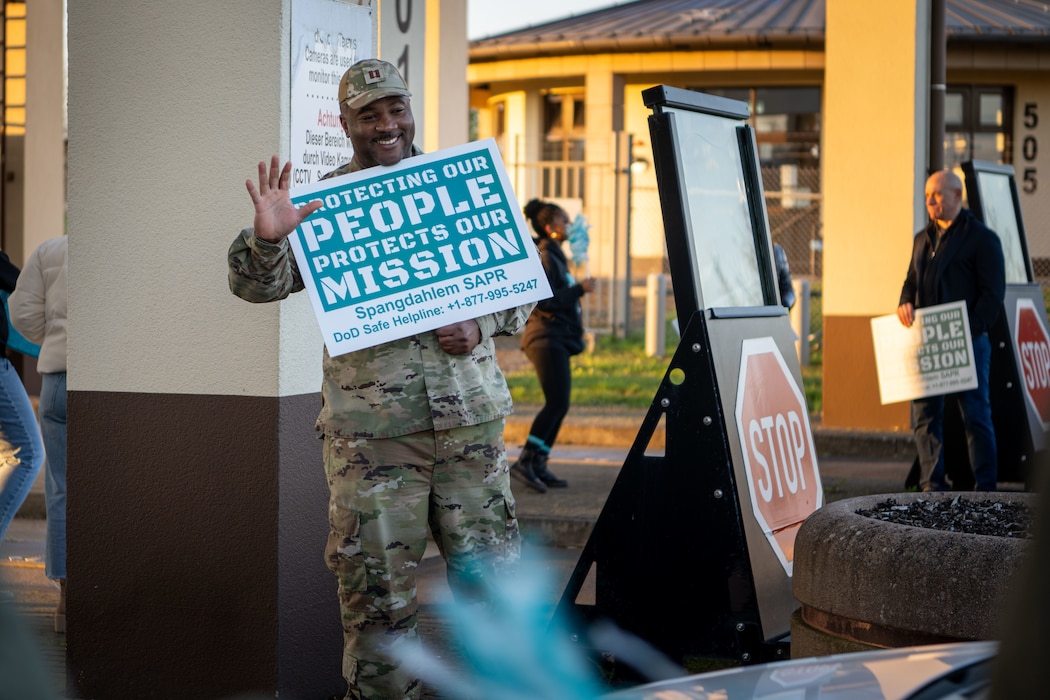 A person holding a Sexual Assault Awareness and Prevention Month sign waves at a service member driving.