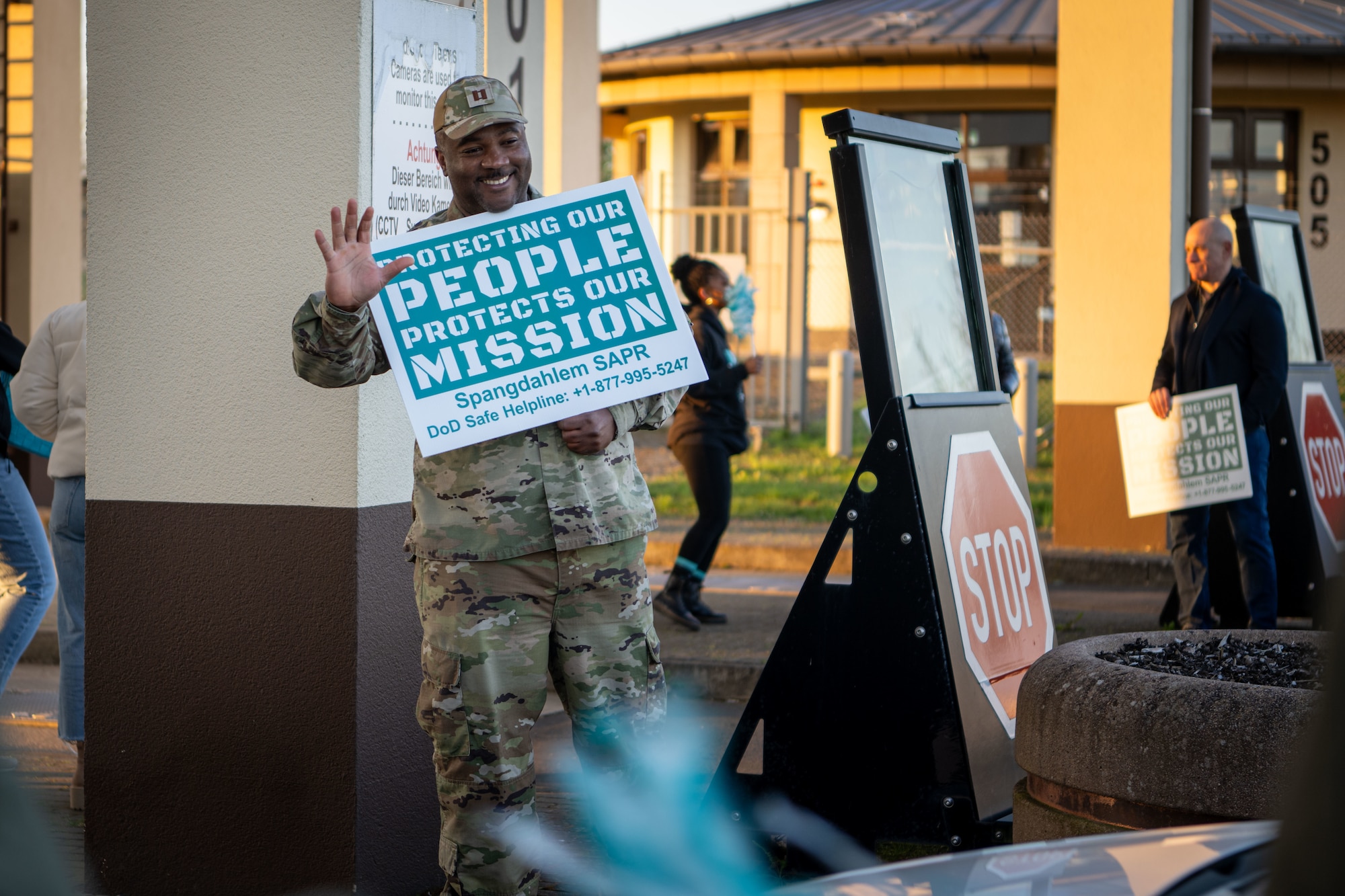 A person holding a Sexual Assault Awareness and Prevention Month sign waves at a service member driving.