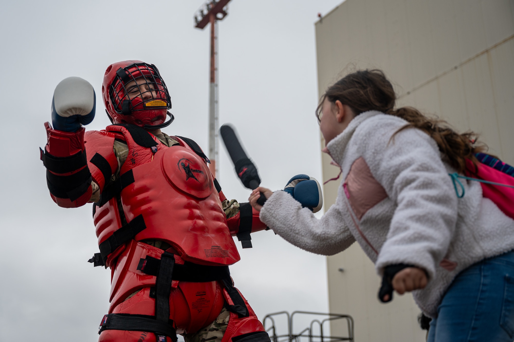 student hits a man in a red man suit with a baton