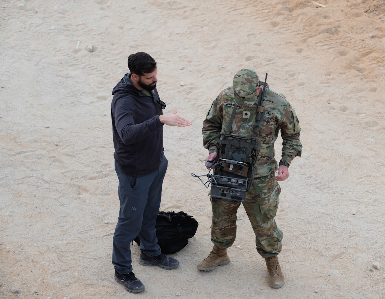 A man in uniform uses a large remote around his neck. A man in regular attire to his left talks to him.