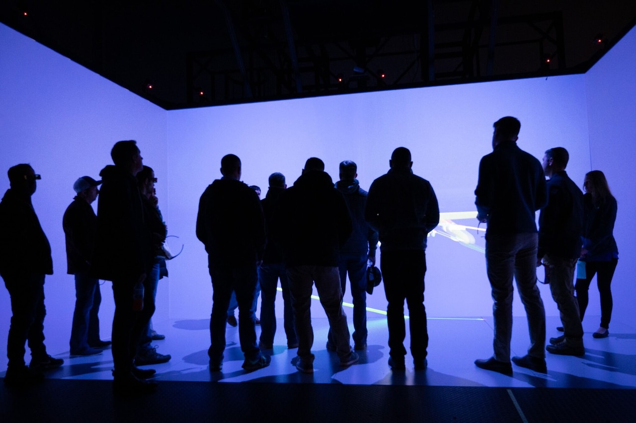 Silhouetted men and women stand in a neon purple room.
