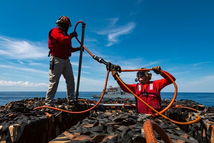 Lt. j.g. Omar DeJesus (left) and Chief Aviation Ordnanceman Thomas Amyx, both assigned to weapons department, attach a pogo stick to a cargo net during a vertical replenishment (VERTREP) on the flight deck of the world's largest aircraft carrier, USS Gerald R. Ford (CVN 78), March 27, 2025.