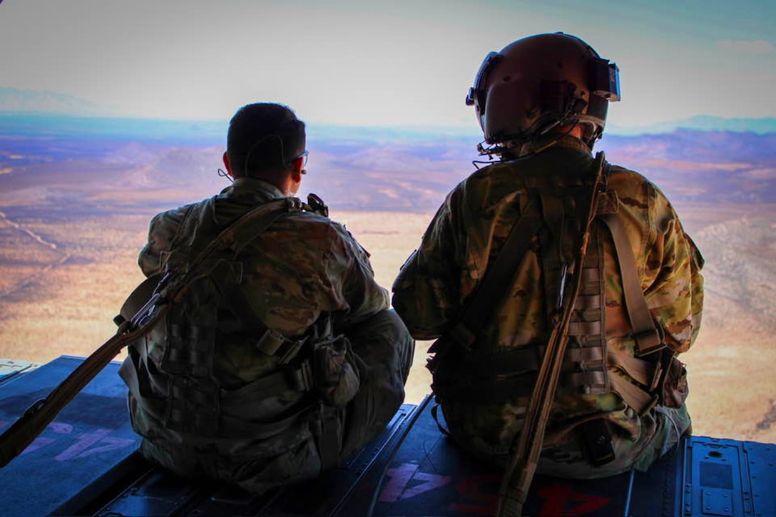 Two soldiers look out at a vast plain from high up.
