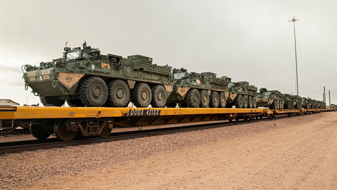 A row of military vehicles sit on a train.