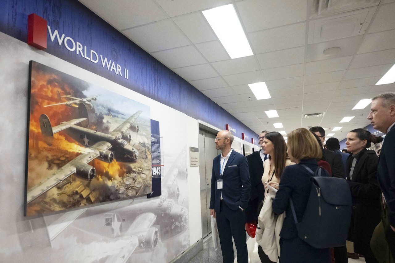 A group of people wearing business attire stands in a hallway. A sign says, "World War II."