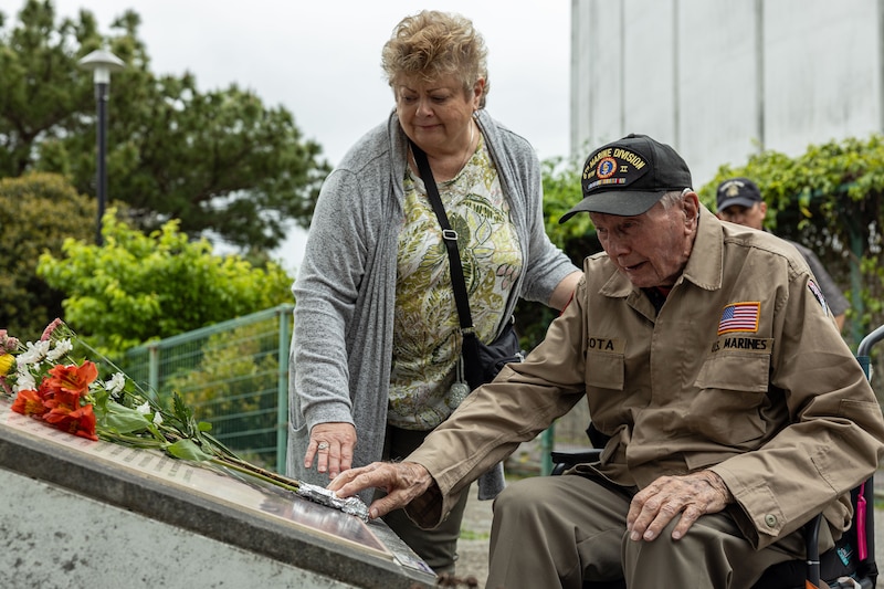 A man and a woman place flowers on a stone plaque outside.