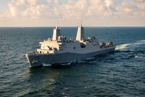 A military ship sails at sea during a partly-cloudy day.