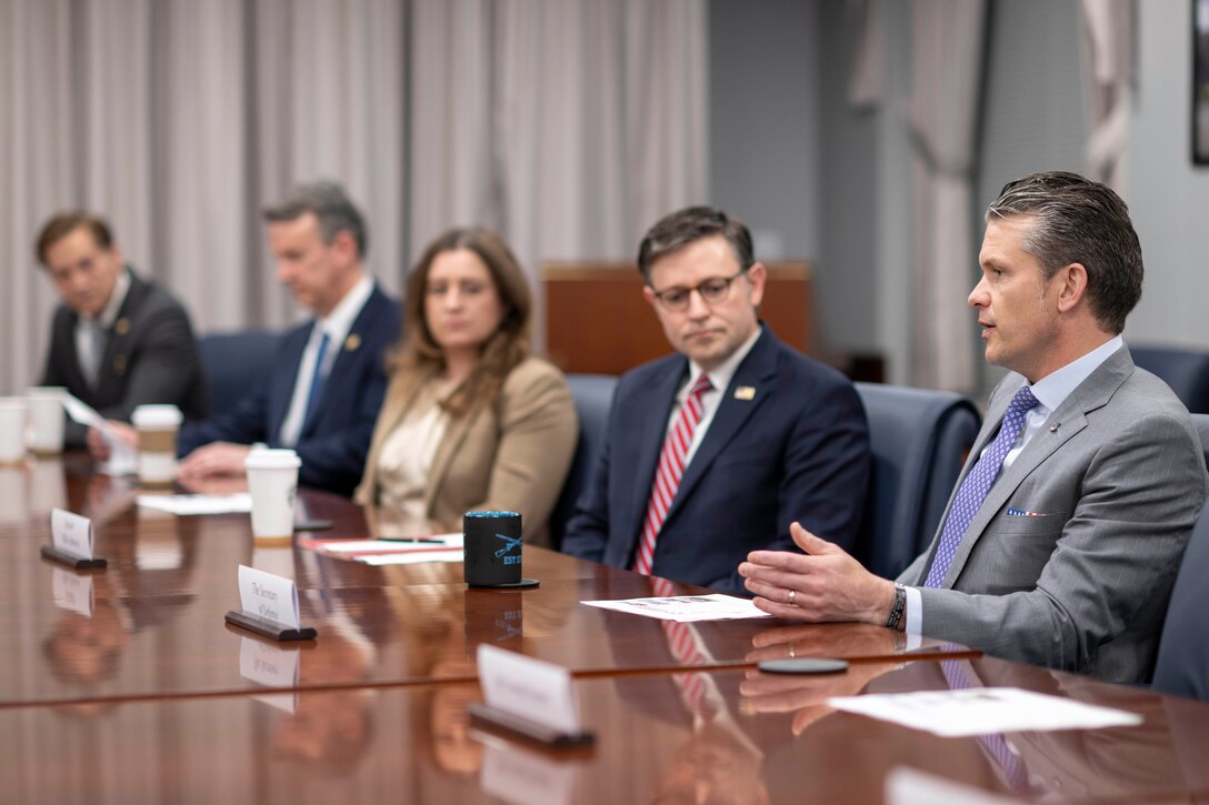 Four people in business attire sit around a table and listen to a man at the table speak.