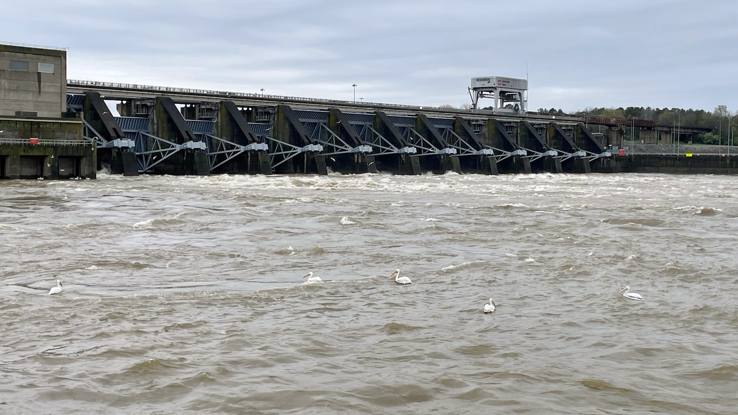 A dam spilling water, looking from near the surface of the river downstream.