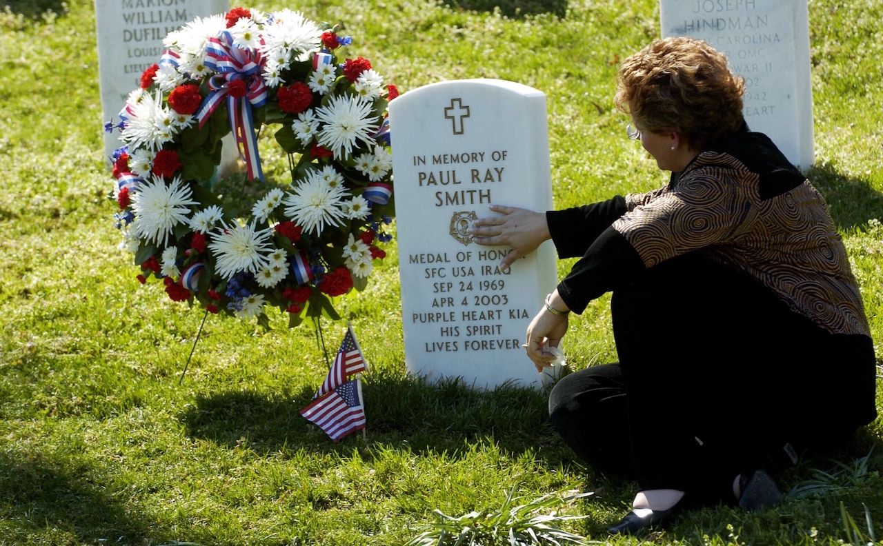 A woman sitting beside a grave places her hand on a headstone.
