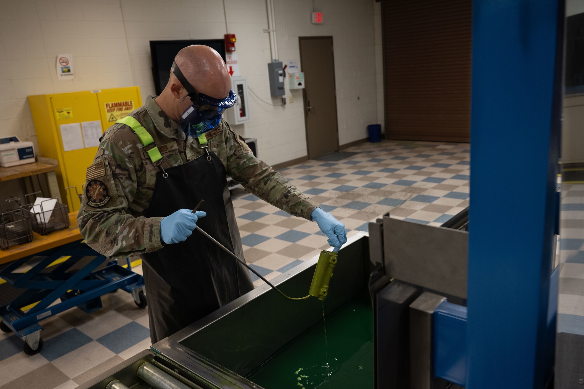 Master Sgt. Jason Barker, 931st Maintenance Squadron nondestructive inspection section chief, dips a KC-135 Stratotanker part in liquid penetrant April 1, 2025, at McConnell Air Force Base, Kansas. Liquid penetrant seeps into any cracks in a metal or non-porous object and glows under ultraviolet light, making any flaws visible when inspected. (U.S. Air Force photo by Airman 1st Class Paula Arce)