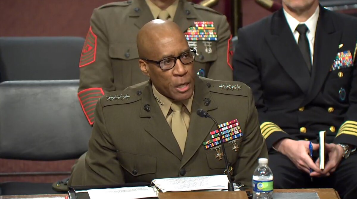 A man in a service uniform speaks from a table.