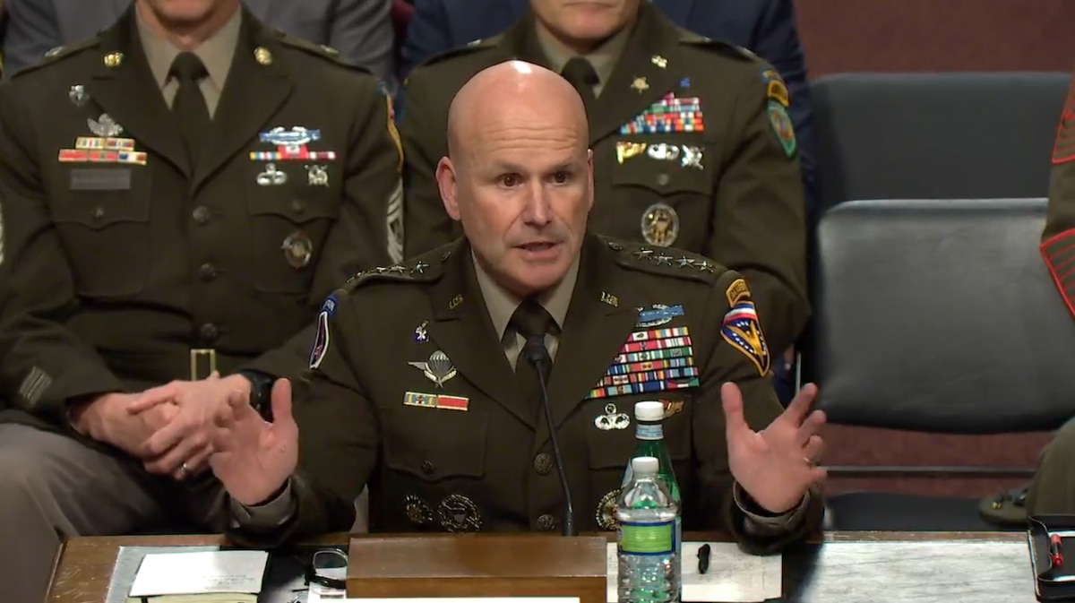 A man in a service uniform speaks from a table.