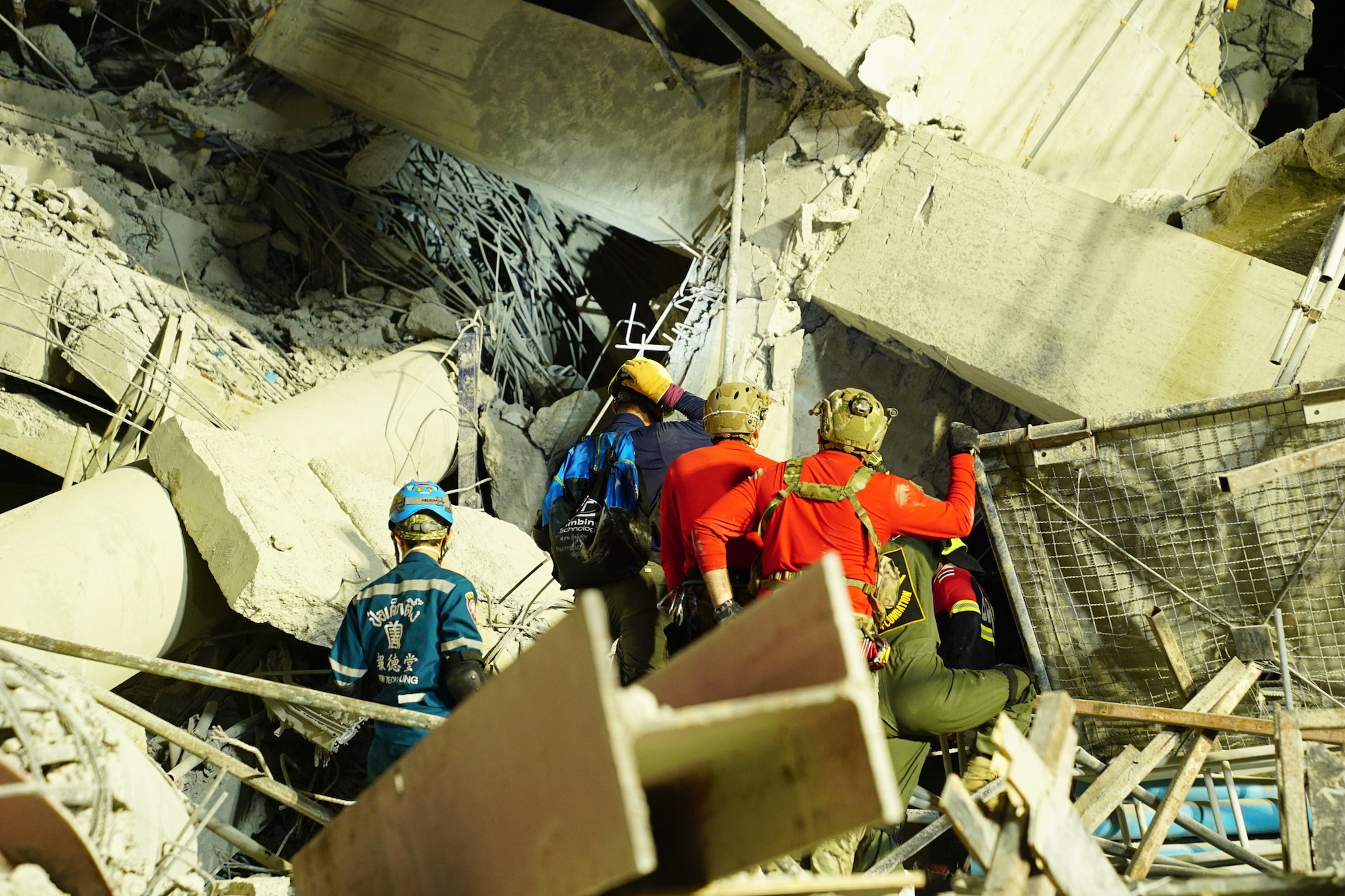U.S. and Thai personnel wearing safety gear examine the debris of a collapsed building.
