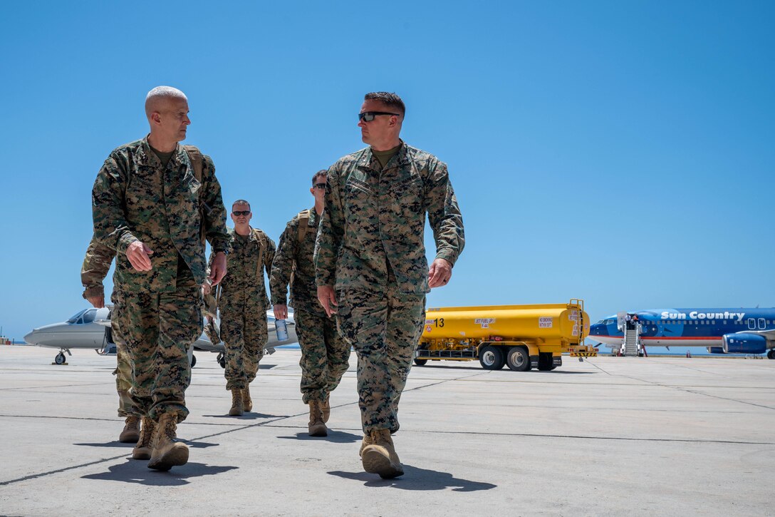 A general walks with a soldier on tarmac in an airfield during a clear day.