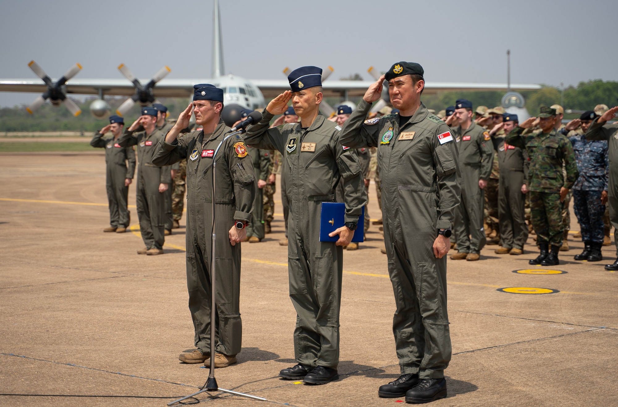 Partner military members stand at attention and salute on the flight line.