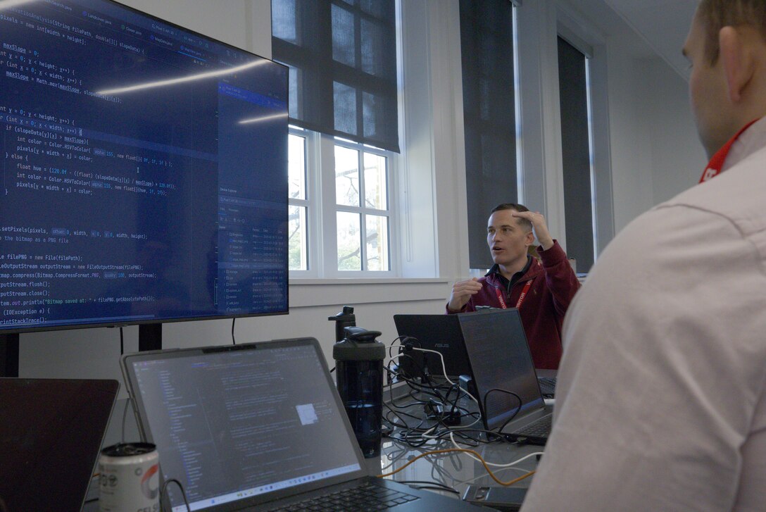 U.S. Marine Corps Capt. Eric Wikman, assigned to the Marine Innovation Unit (MIU), discusses updates to the Augmented Reconnaissance and Estimate of the Situation (ARES) software application at the Marine Corps Software Factory (MCSWF) in Austin, Texas, 17 - 29 March, 2025. MIU Marines are assisting MCSWF in the development and production of software solutions that address critical needs for the Marine Corps, including an update to ARES that predicts helicopter landing zones based on topographical data. MIU is a Selected Marine Corps Reserve unit headquartered in Newburgh, N.Y. that accelerates the development and adoption of advanced capabilities across the Marine Corps. Wikman is a native of Huntsville, Alabama. (U.S. Marine Corps photo by Cpl. Orion Stpierre)