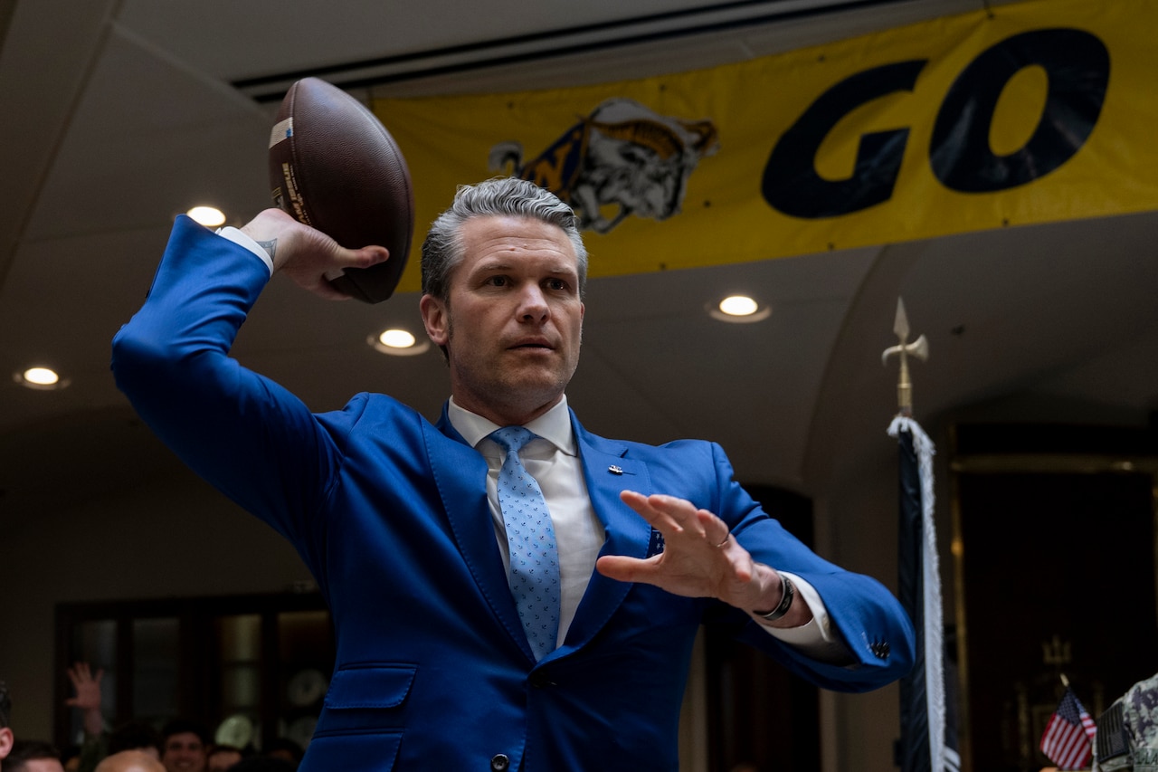 A man in a suit holds a football above his shoulder ready to toss it.